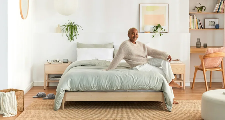 Ash Zen bed base with green linen and a person sitting on the bed in a staged bedroom.